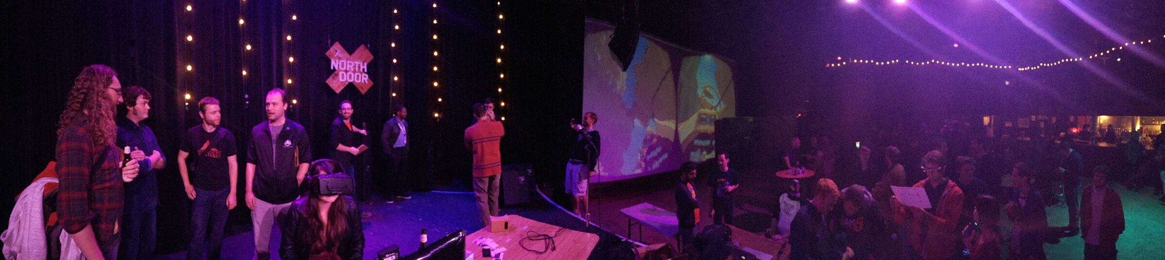 Panoramic view of the 2014 Austin VR meetup at The North Door, with PolyFish projected on a large screen and attendees watching